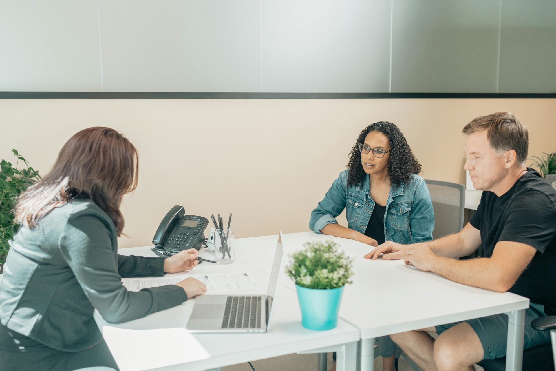Anonymous female employee interacting with diverse clients at table with netbook and paper sheet in workspace